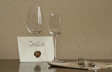 Image of empty whine glasses with an envelope leaning against one