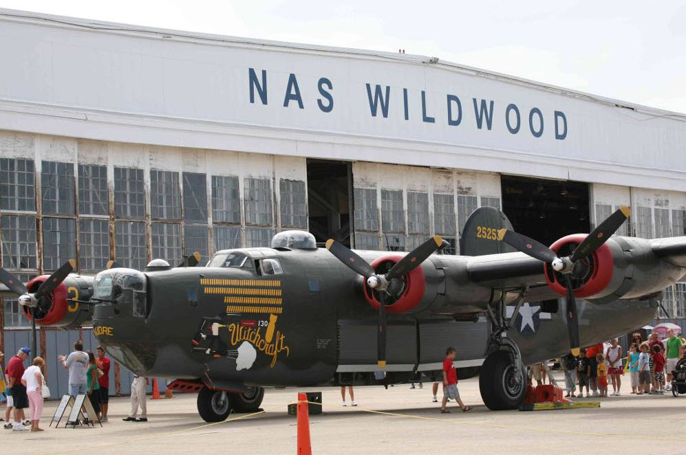 old warplane that is green with red accents in front of a plane hangar that says nas wildwood