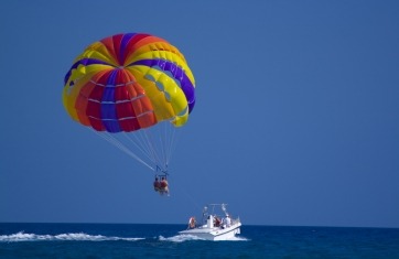 Paragliders being pulled by a boat with a rainbow parachute
