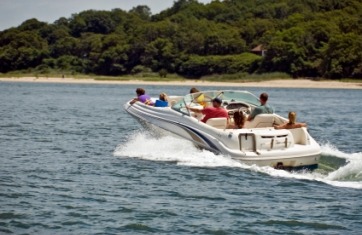 family on a speed boat on the water moving away from the camera with a back and trees in the background