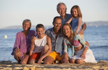 A family including grandparents, parents and a son and daughter on a beach posing and smiling.