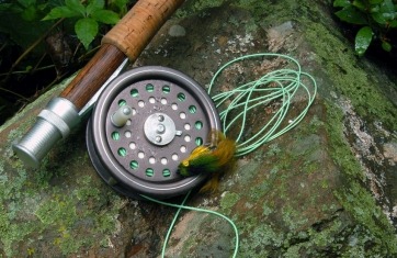 Closeup of fly fishing real with green string and a green and yellow lure