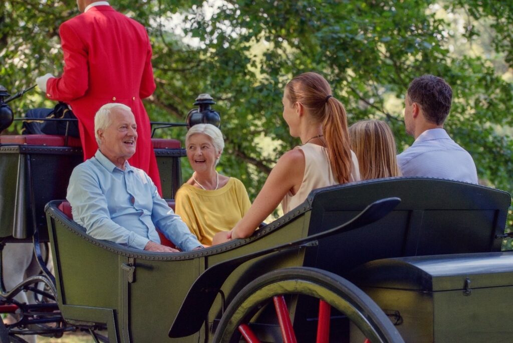 Five people including a grandma and a grandpa and a father and a daughter and mom in a carriage with a man in a red jacket driving it.