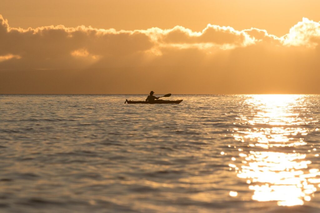 person kayaking on the water with he sun rising