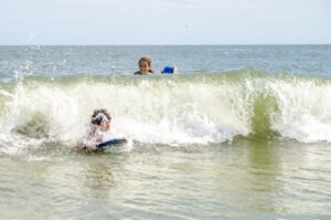 Teenage girl and boy surfing into Atlantic Ocean with small surfing board during summer day