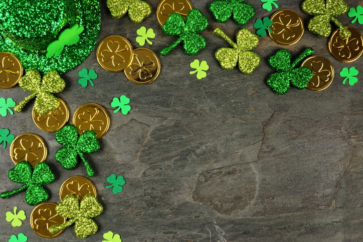 St Patricks Day corner border with shamrocks, gold coins and leprechaun hat over a dark slate background